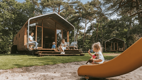 Ouders zitten met hun peuter voor hun wikkelhouse bij vakantiepark Beerze Bulten. De dochter is net van de glijbaan gegleden en zwaait naar haar ouders.