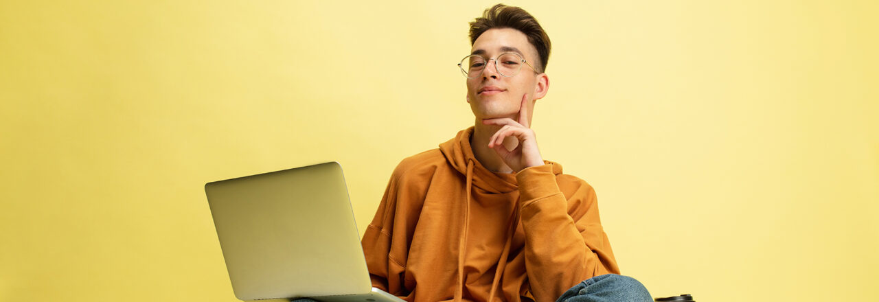Een student zit in kleermakerszit met een laptop op schoot