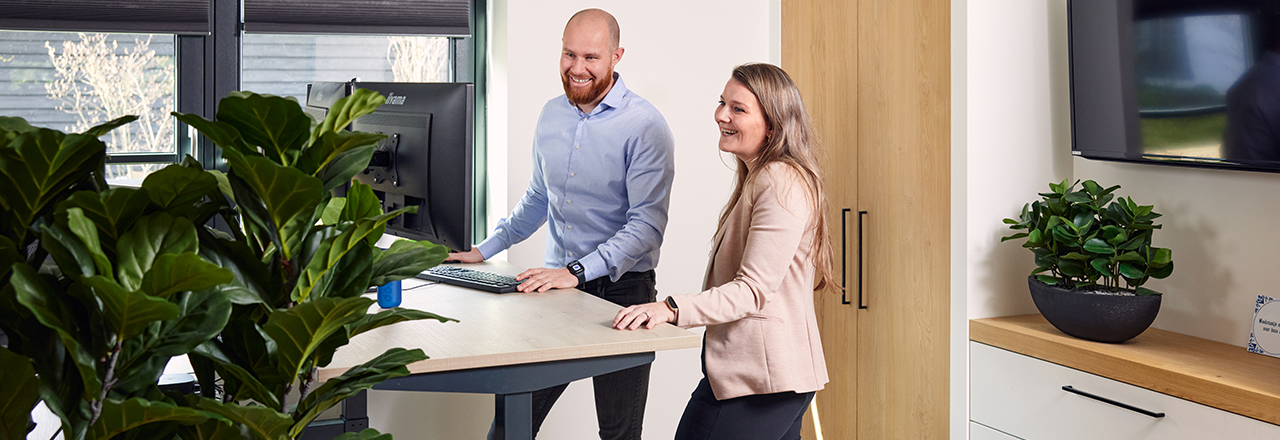 Twee Wentzo collega staan lachend achter een bureau en kijken naar een computerscherm
